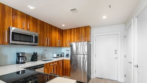A modern kitchen with wooden cabinets, stainless steel appliances, and a white door. - Sophisticated 1BR Living w Pool in NOLA (New Orleans)