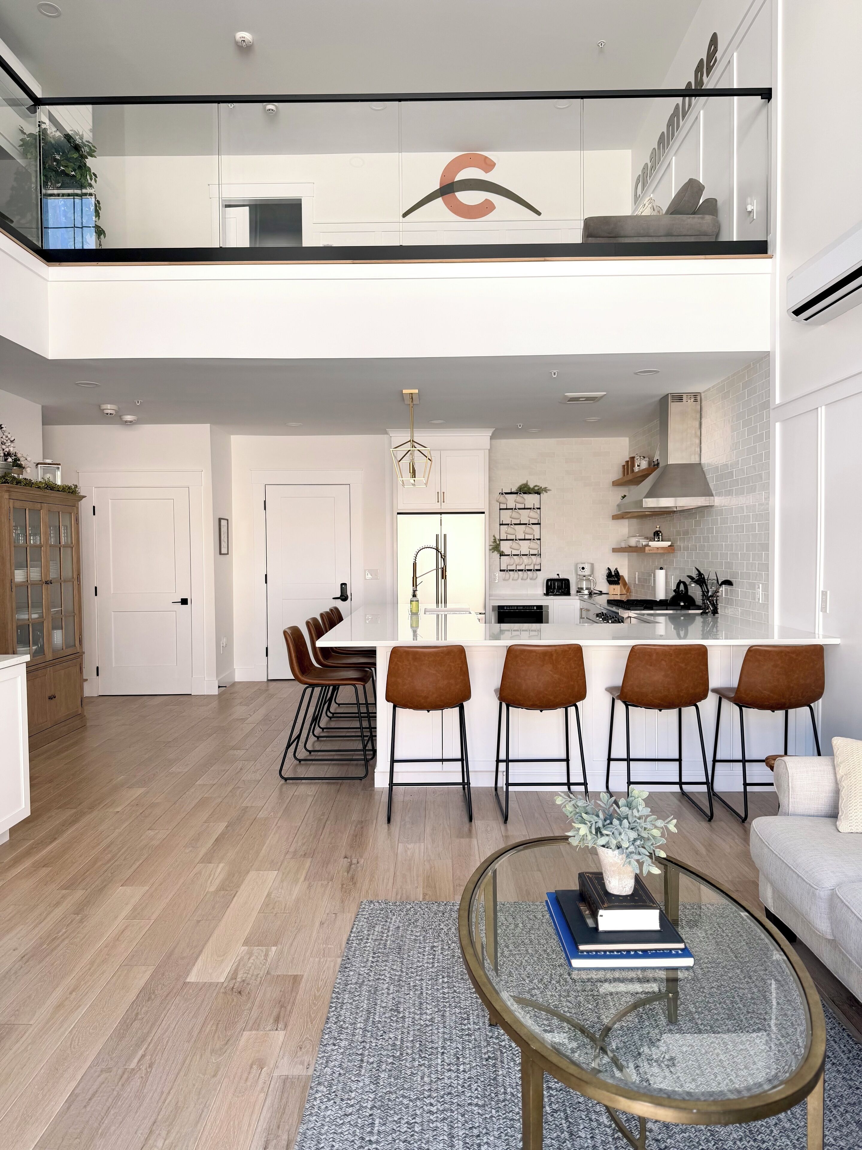 A modern kitchen with a central island, bar stools, and a dining area with a glass table.