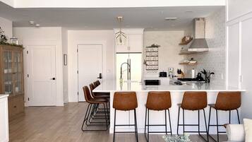 A modern kitchen with a central island, bar stools, and a dining area with a glass table.