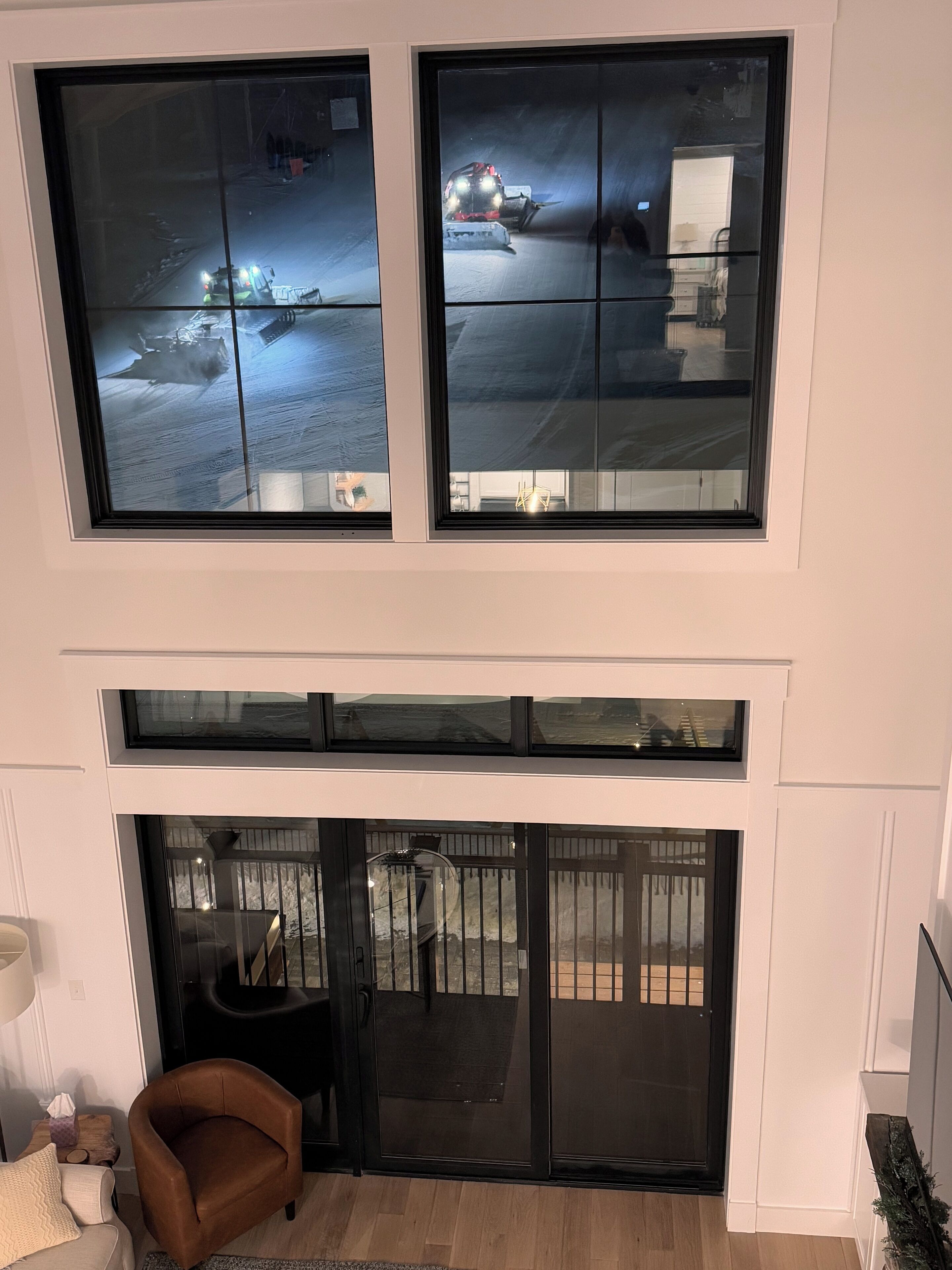 A modern interior with a high ceiling, large windows, and a sliding glass door leading to an outdoor area.