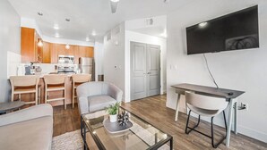 A modern living room with a glass coffee table, a grey sofa, and a dining area with a small table and chairs. - Landing | Spectacular 1BD, Courtyard, Pool (Salt Lake City)