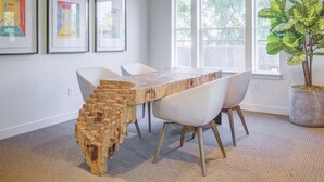 Un comedor moderno con un banco de madera original, sillas blancas y un ventanal con vistas a árboles.