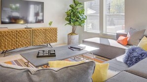 Una sala de estar moderna con un sofá, una mesa de centro y una televisión. Hay una planta y un mueble con diseño texturizado.