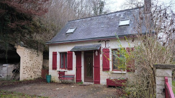 Een rustiek stenen huis met een schuin dak, een klein terras en een bank.
