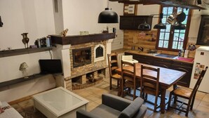 Een gezellige woonkamer met een open haard, een eethoek met houten stoelen, en een keuken met hangende lampen.