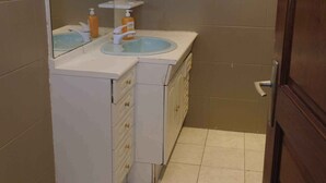 Een badkamer met een wastafel, spiegel en een raam boven de spiegel.