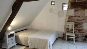 Een slaapkamer met een schuine kap, een bed, een nachtkastje, een stoel en een haard van baksteen.