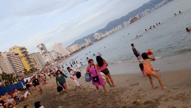 A crowded beach with people walking and swimming, and a cityscape in the background. - Well located, close to everything (Acapulco de Juárez)