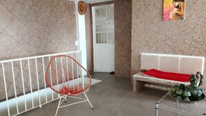 A room with a red chair, a white sofa with a red cushion, a tiled wall, and a door with a white gate. - Well located, close to everything (Acapulco de Juárez)