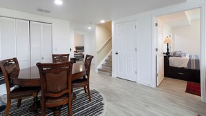 A dining area with a wooden table and chairs, a staircase, and a bedroom with a bed and nightstand.