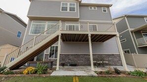 A two-story residential building with a covered porch, stone foundation, and a small outdoor seating area.