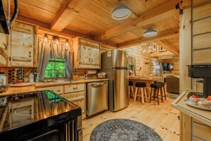 A wooden cabin interior with a kitchen area featuring a refrigerator, stove, and bar stools. - Monarch Mountain Luxury Cabin with Hot Tub Pet Friendly (Elizabethton)