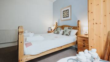 A wooden bed with white linens, a nightstand with a lamp, and a framed picture on the wall.