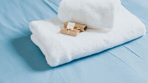 Een keurig opgemaakt bed met een blauwe spreideken en een witte handdoek er bovenop, samen met een klein houten voorwerp.