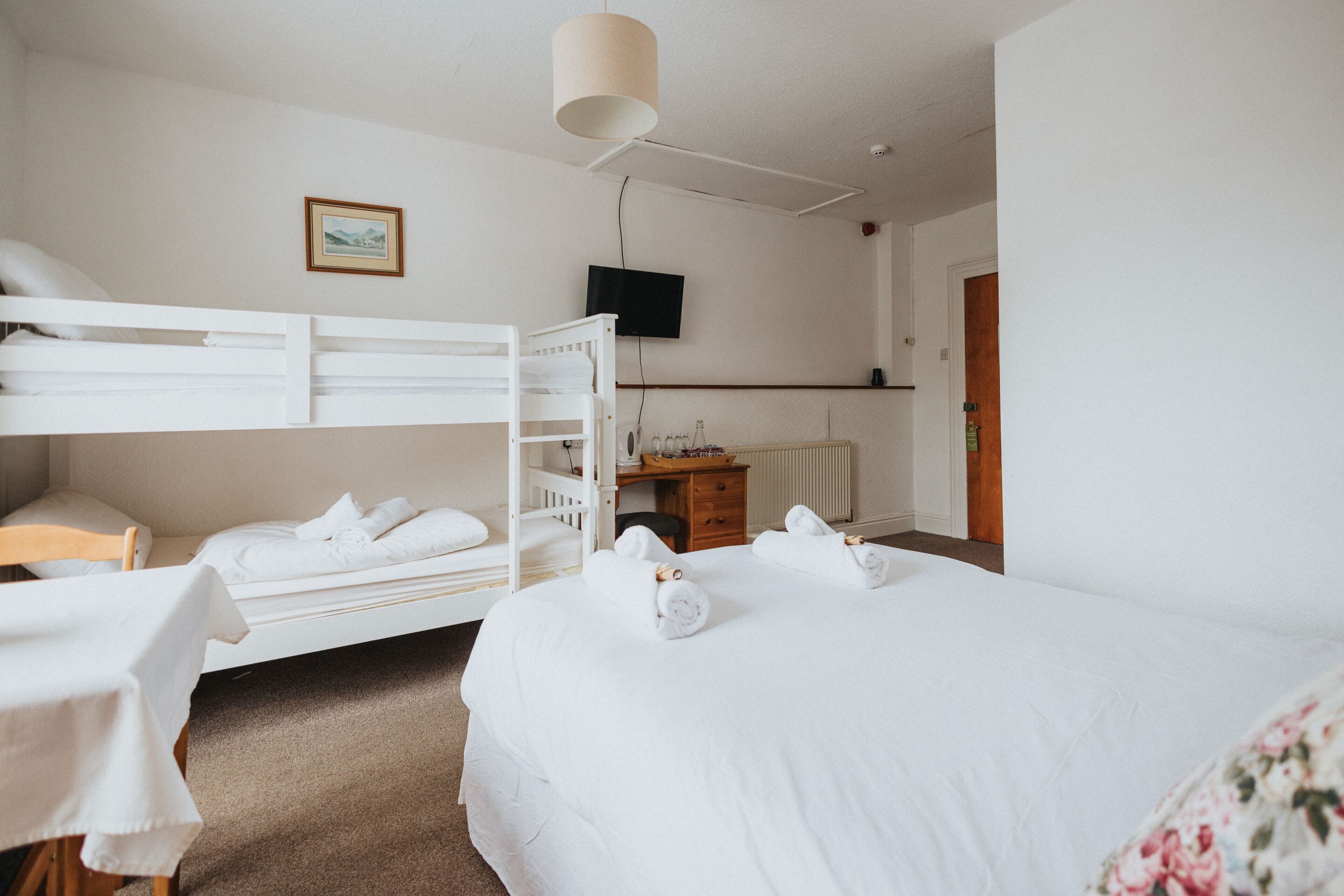 A hotel room with a bunk bed, a desk with a chair, a television, and a bed with towels.