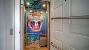 A hallway with a large shark mural, a small bench, and a door with a metal handle. - Coastal Soiree Ocean Views, Game Room, & Steps From Port Aransas Beaches (Port Aransas)