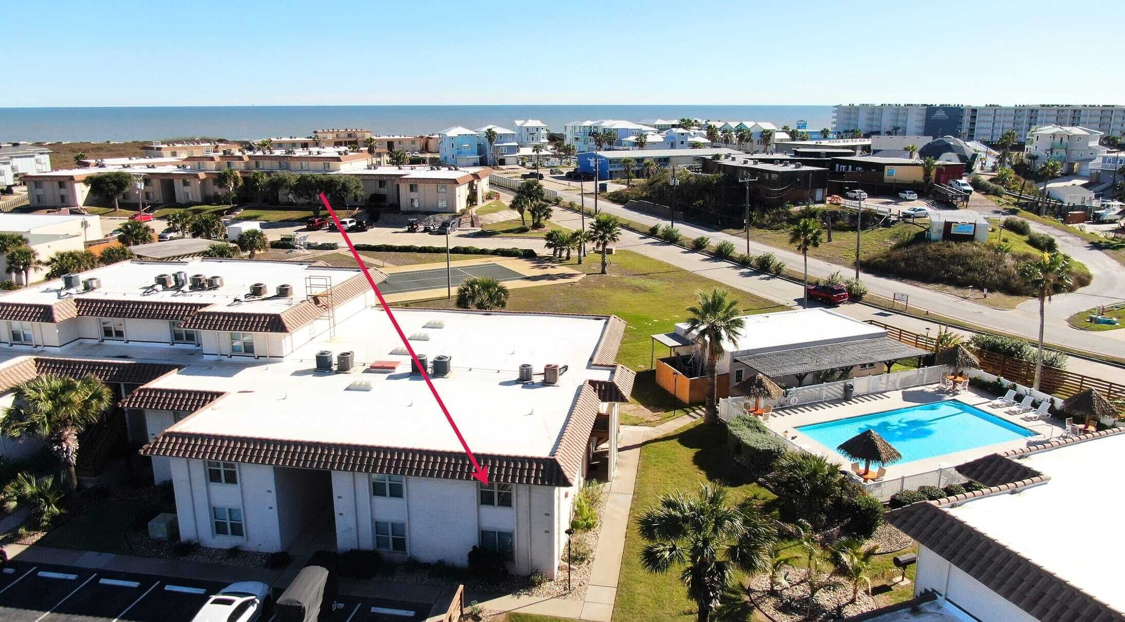 A residential area with a swimming pool, multiple buildings, and a view of the ocean.