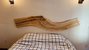 Una cama con colcha escocesa, cabecero de madera y dos lámparas fijadas a la pared.