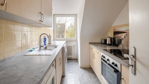 Cocina compacta con lavabo, estufa y horno, con armarios de tonos claros y ventana que proporciona luz natural.