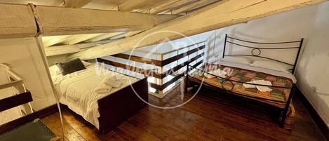 Dormitorio tipo loft con dos camas, vigas de madera y una maleta.