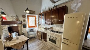 A kitchen with wooden cabinets, a gas stove, a refrigerator, a dining table with a checkered tablecloth, a hanging light fixture, and a stone fireplace. - La Scalinatella "UnaNotteaCasaMia" (SACROFANO)