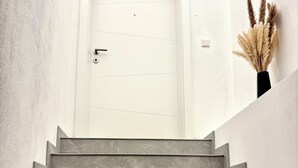 A staircase leading to a white door with a keyhole, a wall-mounted vase with pampas grass, and a textured wall. - "Seeblick" guest house - Bright penthouse apartment on the outskirts of Salzburg (Seekirchen am Wallersee)