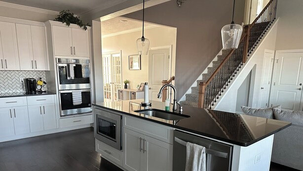 A modern kitchen with white cabinetry, stainless steel appliances, and a dark countertop. - Master's Tournament Rental House (Grovetown)