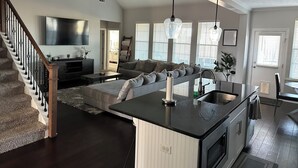A spacious living area with a large sofa, a kitchen island, and a staircase. - Master's Tournament Rental House (Grovetown)