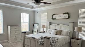 A bedroom with a bed, dresser, nightstands, a ceiling fan, and a wall sign. - Master's Tournament Rental House (Grovetown)