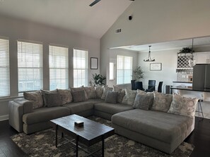 A modern living room with a sectional sofa, a coffee table, and a dining area with a chandelier.
