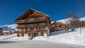 Un chalet en bois à plusieurs étages, doté de balcons, qui se dresse sur fond de montagnes enneigées.
