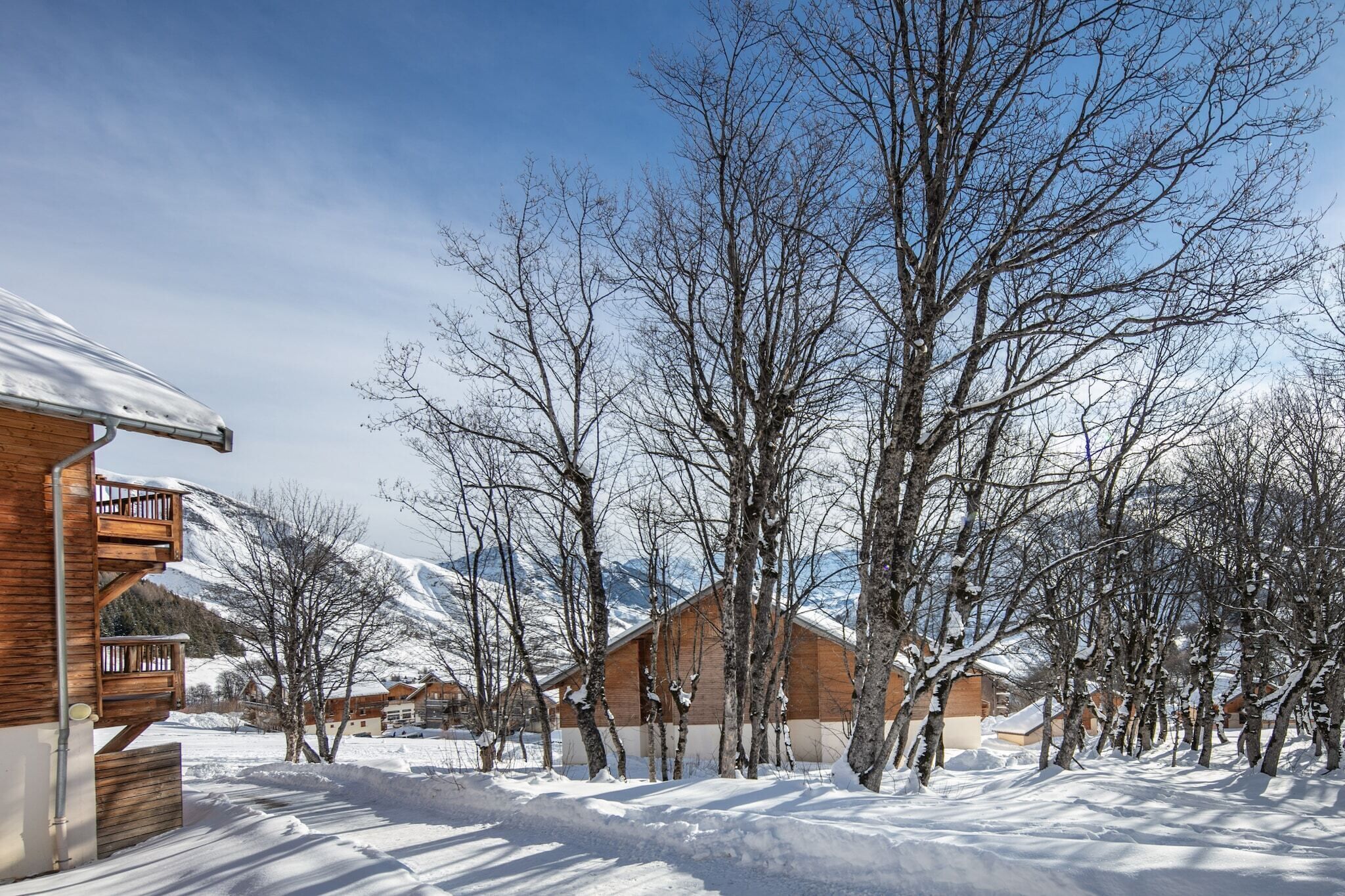 A snow-covered landscape with wooden cabins and bare trees.