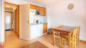 A compact kitchen with wooden cabinets, a microwave, and a sink. There is a dining table with chairs and a clock on the wall. - Les Grizzlis N°27 - 2P6C (Saint-Sorlin-d´Arves)
