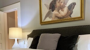 Una cama bien hecha con cabecera, una lámpara de noche y una obra de arte enmarcada encima.