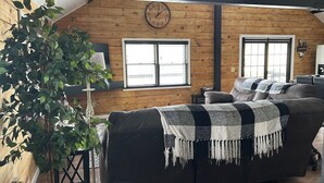 Ein gemütliches Wohnzimmer mit Holzbalkendecke, einer großen Uhr und einem Sofa mit Decke.