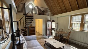 Een ruime loft met hoge plafonds, een trap naar een hoger niveau, een eethoek met tafel en stoelen, en een gezellige zithoek met een bank en salontafel.