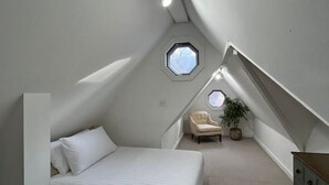 Een kamer met een laag, schuin dak, een bed, een stoel, een dressoir en een dakraam.