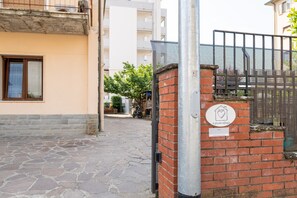 Une rue pavée de pierres, un mur de briques avec un portail en métal et un bâtiment doté d’une fenêtre et d’une enseigne.