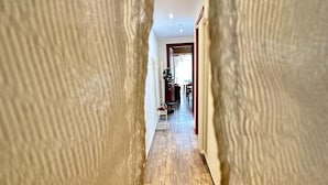 Un pasillo con suelo de madera, una silla blanca y un comedor al fondo.