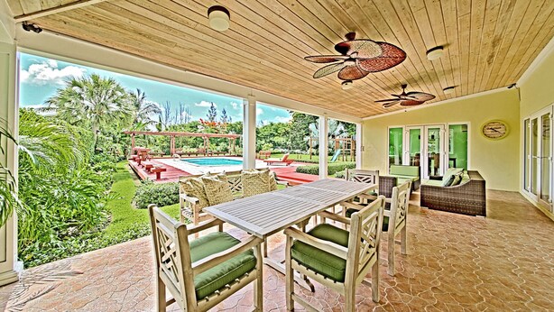 Una veranda coperta con piscina, mobili da esterno e vista su un giardino rigoglioso.