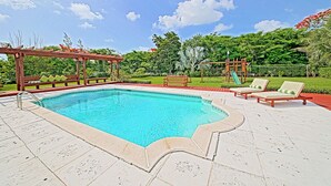 Una piscina con una pergola in legno e lettini prendisole, immersa in un giardino curato e con un'area giochi.