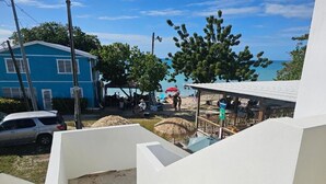 A beachside property with a blue house, a covered seating area, and a view of the ocean. - Buye Apartments (Cabo Rojo)