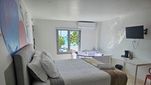 A modern bedroom with a large bed, a desk, and a TV. - Buye Apartments (Cabo Rojo)