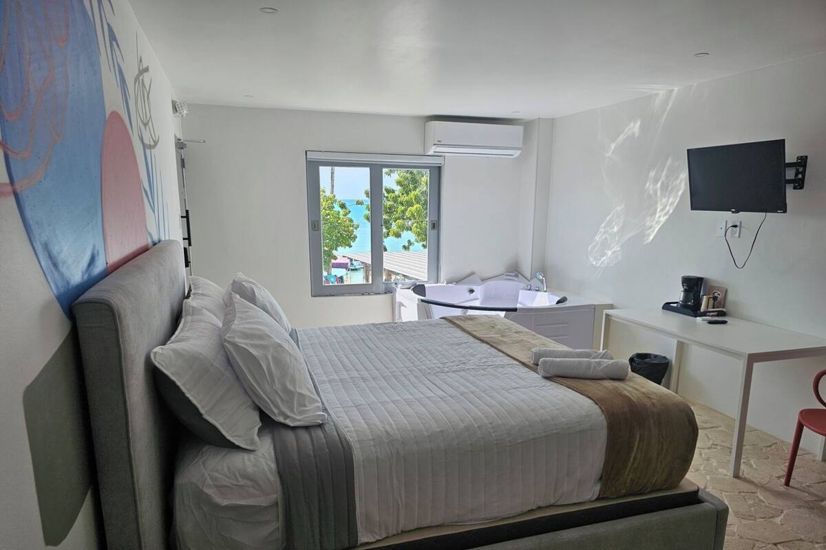 A modern bedroom with a large bed, a desk, and a TV.