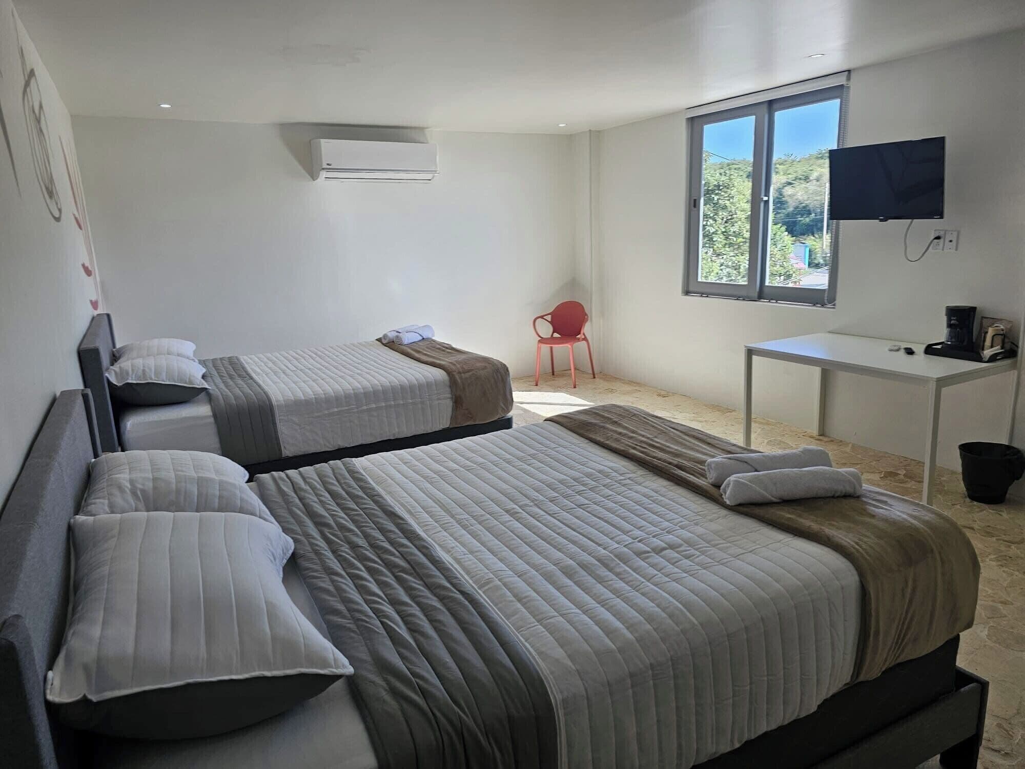 A room with two beds, a desk, a chair, and a TV.