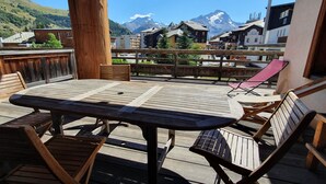 A wooden deck with a table and chairs, overlooking a mountain range and a town. - Alpine Comfort for 8 guests (Les Deux Alpes)