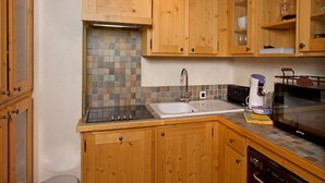 A compact kitchen with wooden cabinets, a tiled backsplash, a sink, a stove, a microwave, and a coffee maker. - Getaway for 10 Near Slopes (Les Deux Alpes)