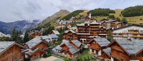 A cluster of wooden chalets with sloped roofs, set against a backdrop of mountains and a cloudy sky.