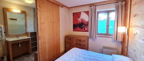 A bedroom with a bed, a wooden dresser, a mirror, and a window with curtains.