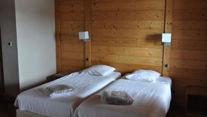 Una habitación con dos camas individuales, paredes de madera y dos lámparas fijadas a la pared.